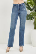 Blue jeans worn by a person on a white background with a plant in the corner