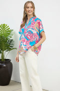 Woman wearing a colorful patterned top and white pants on a white background