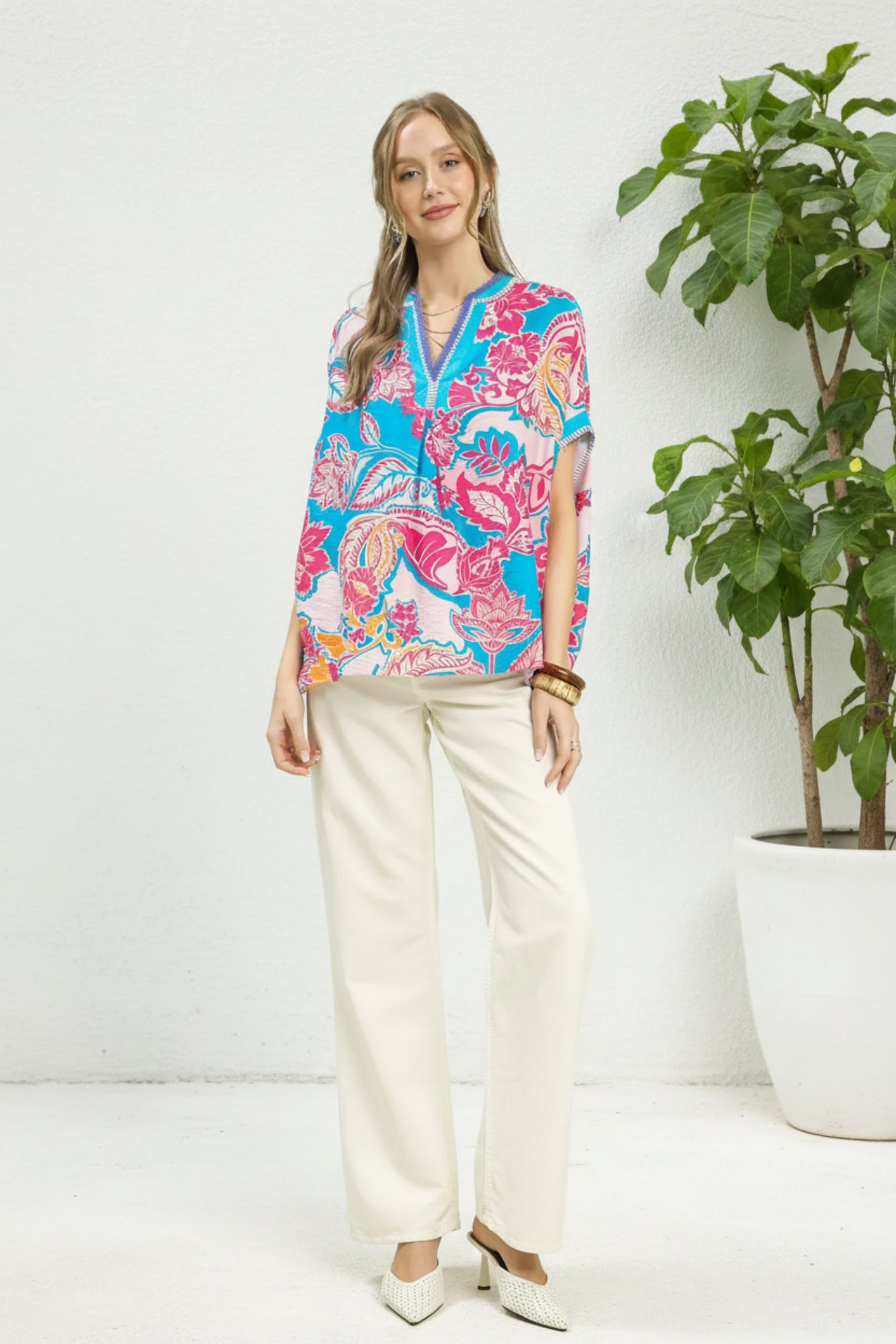Woman wearing a colorful patterned blouse and white pants on a White background