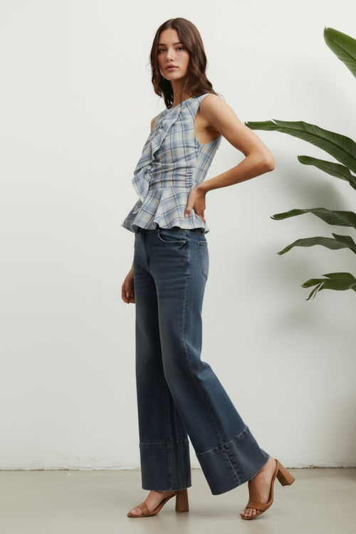 Woman wearing a plaid top and dark blue jeans against a white background