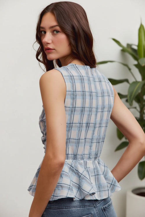 Woman wearing a blue plaid peplum top against a pink background