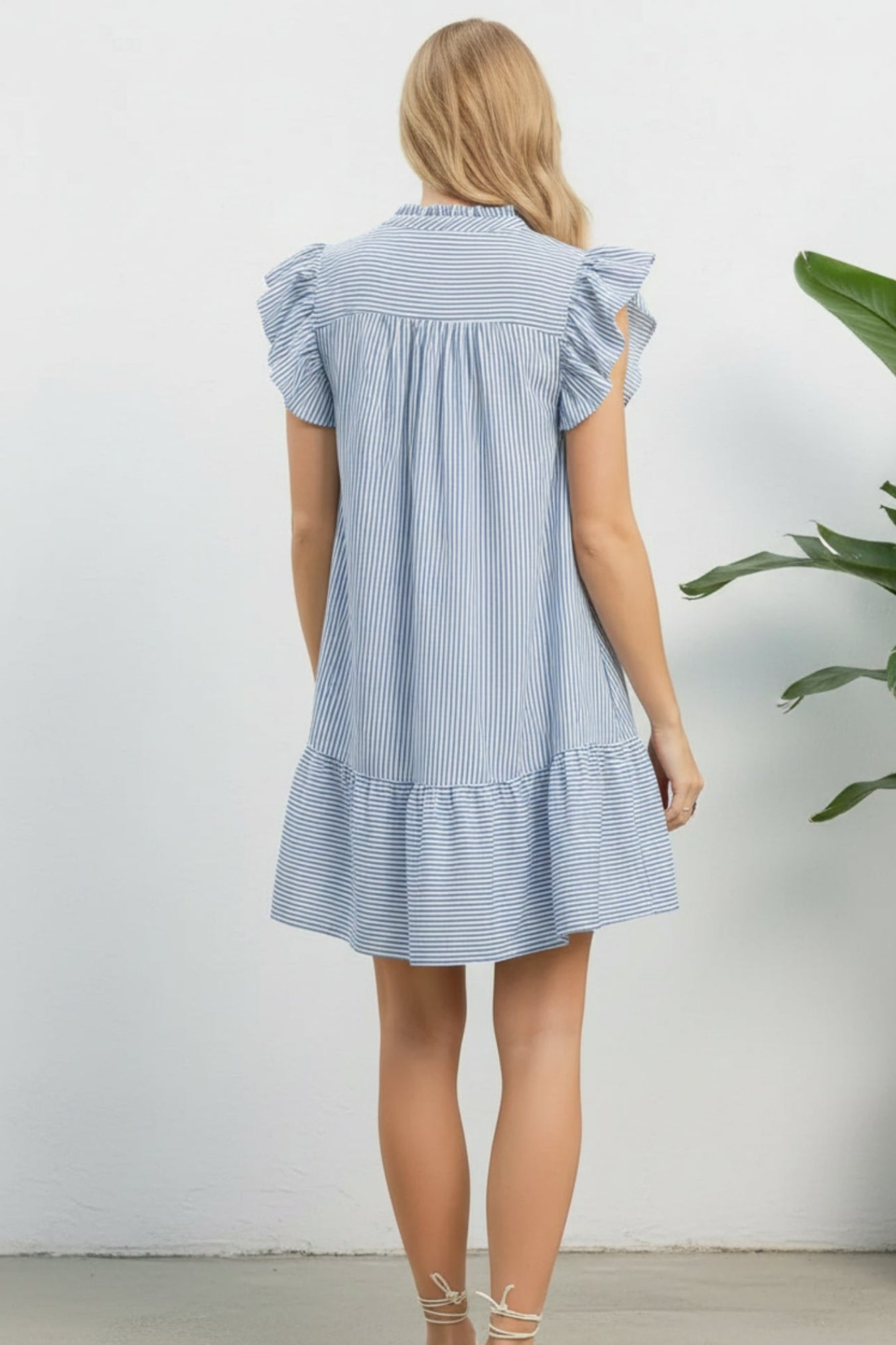 Woman wearing a blue and white striped dress on a white background with plant on the side