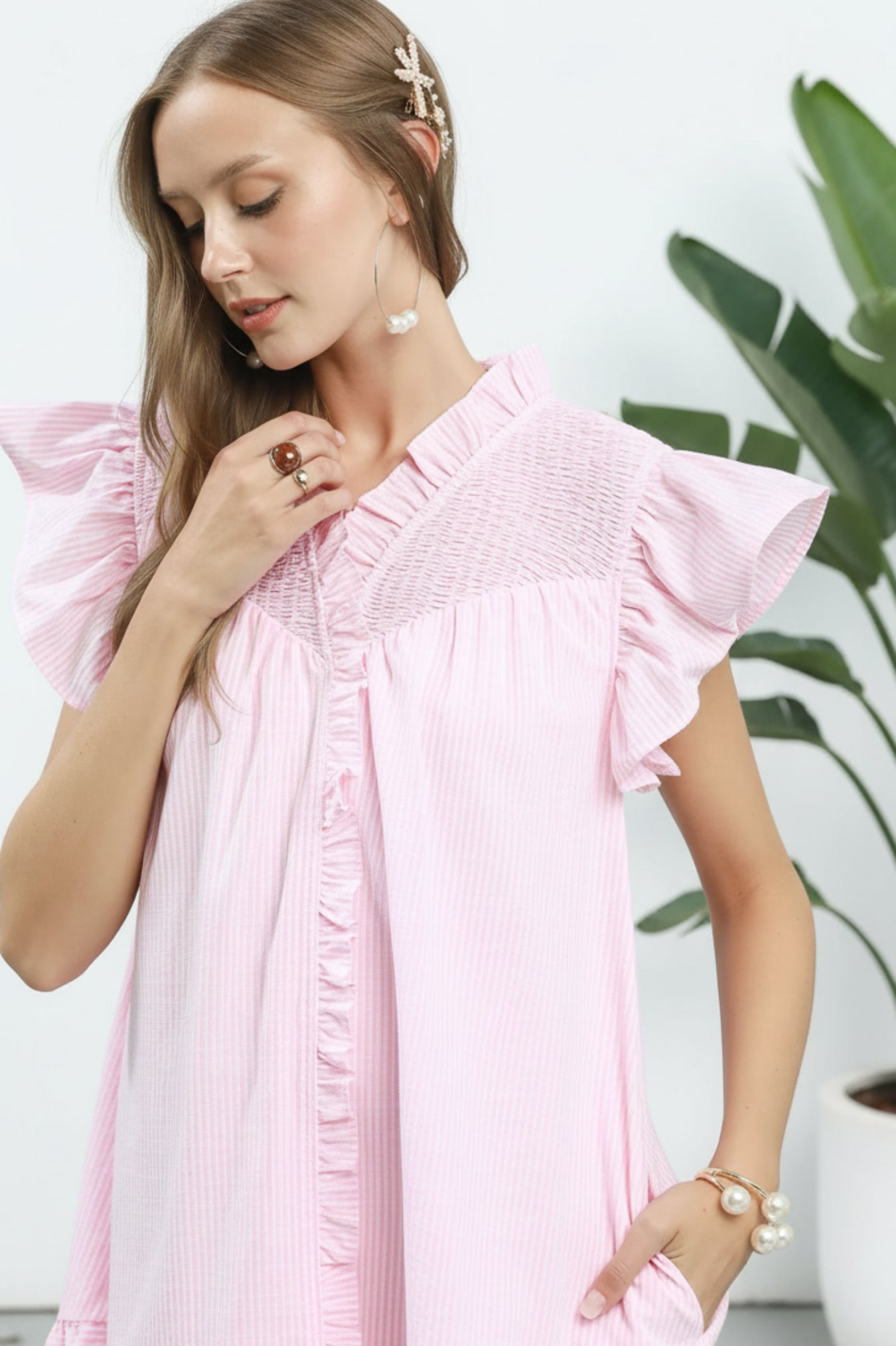 Woman wearing a pink dress with ruffled sleeves against a white background