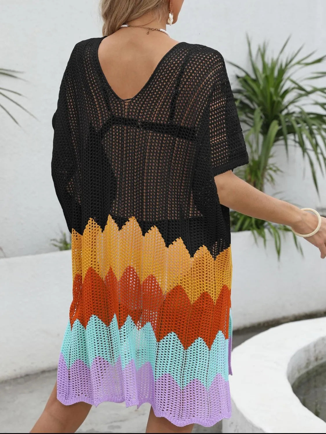 Black crochet cover-up with colorful gradient pattern worn by a person outdoors.