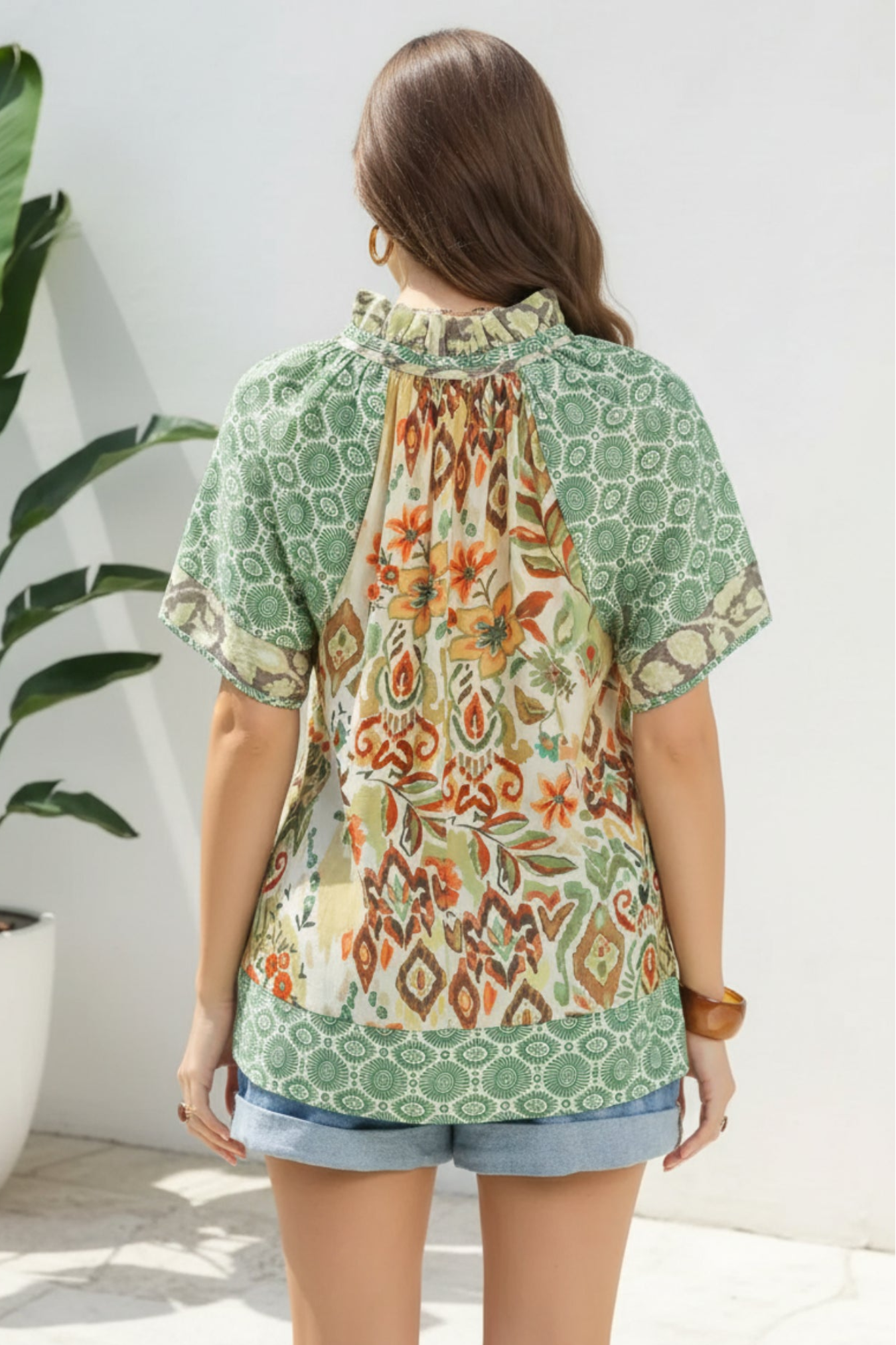 Woman wearing a green patterned blouse with a plant in the background