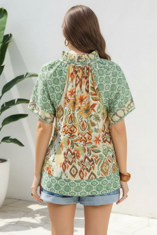 Woman wearing a green patterned blouse with a plant in the background