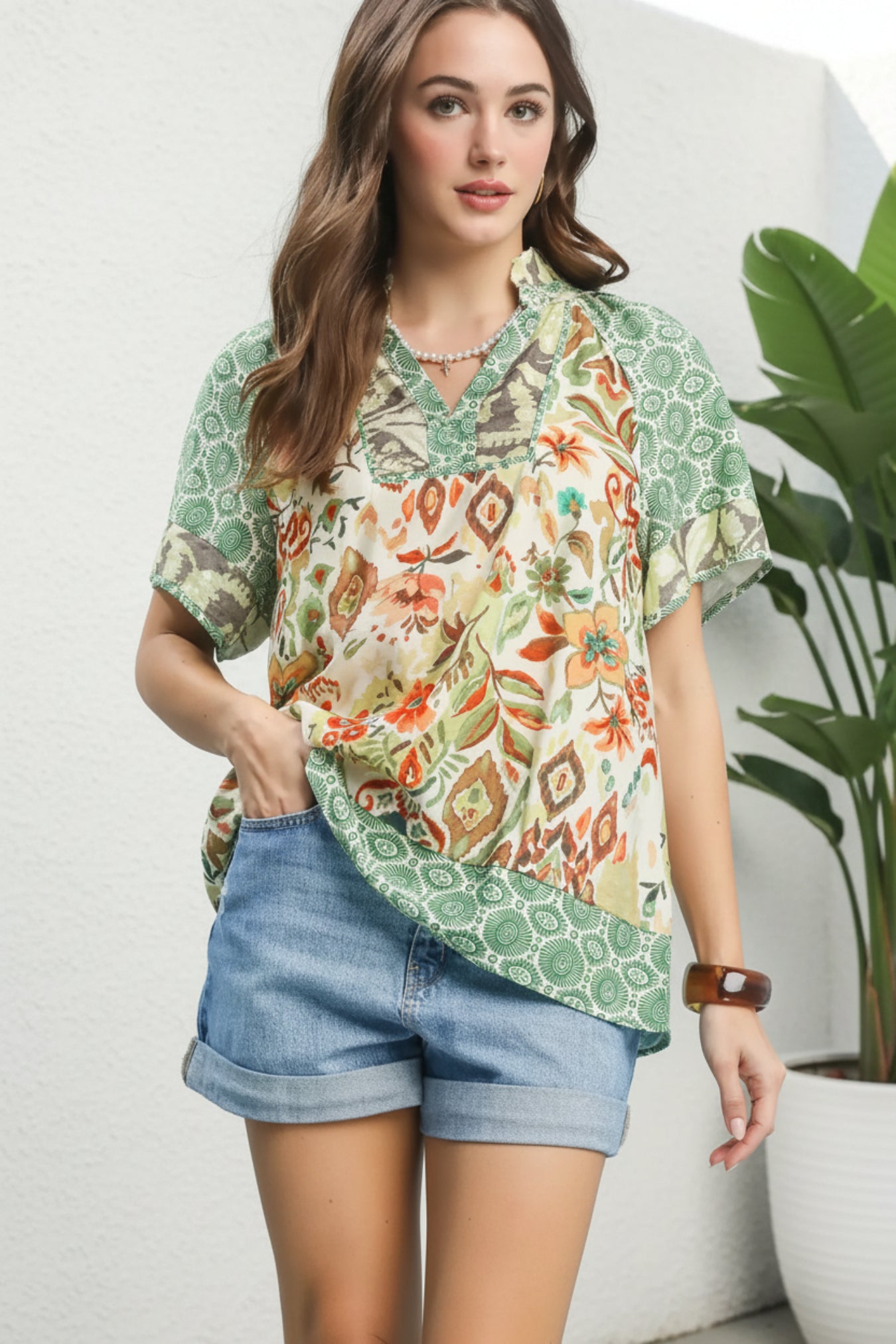Woman wearing a patterned blouse and denim shorts on a plant white background