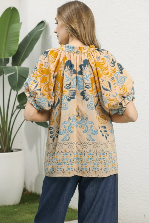 Woman wearing a patterned blouse with puff sleeves against a plant and white background