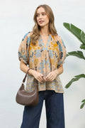 Woman wearing a patterned blouse and holding a brown bag against a white background
