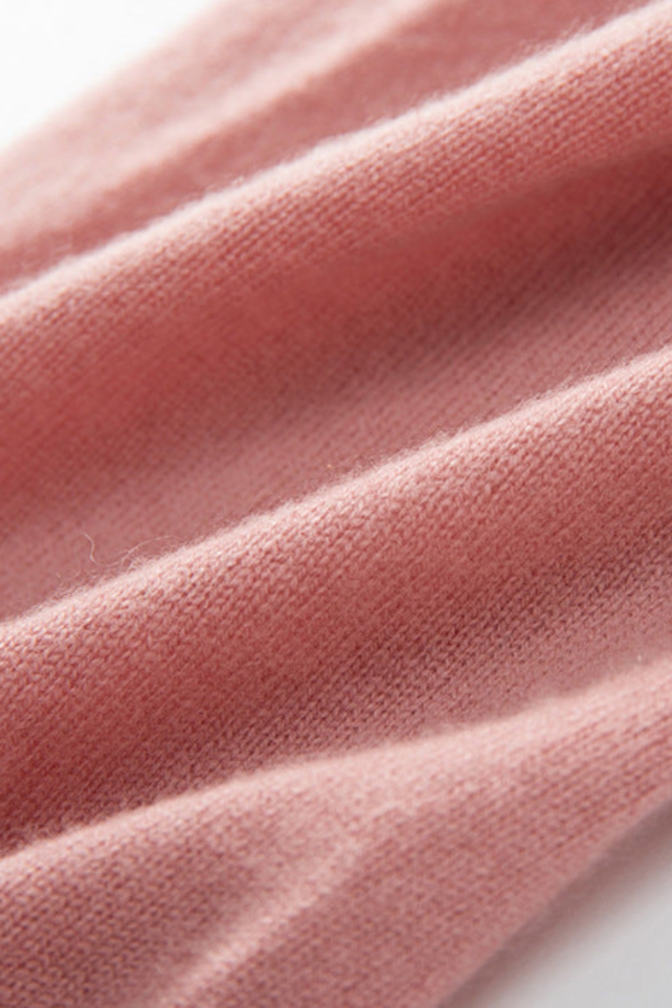 A close-up of draped dusty pink knit fabric with soft folds and a fine ribbed texture on a white background.