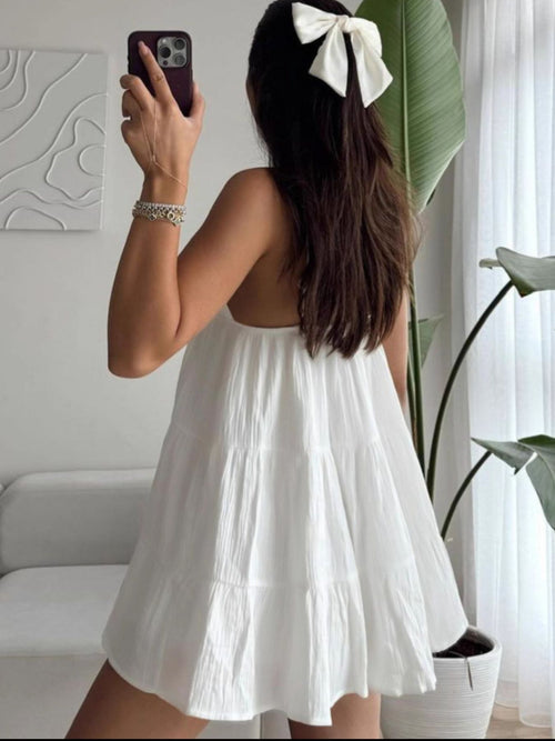 Woman in a white dress taking a mirror selfie in a bright room with plants.