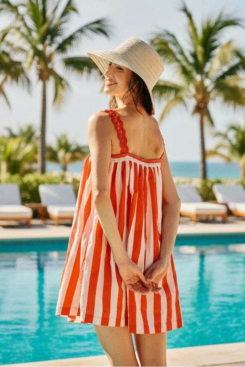 Woman wearing a red and white striped dress with a straw hat outdoors.