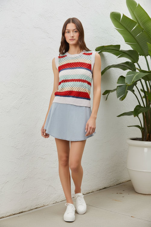 Woman wearing a colorful sleeveless top and light blue skirt on a white background next to a plant