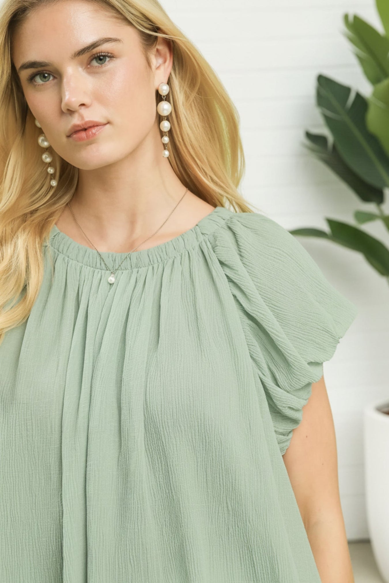Woman wearing a light green dress with pearl earrings indoors.