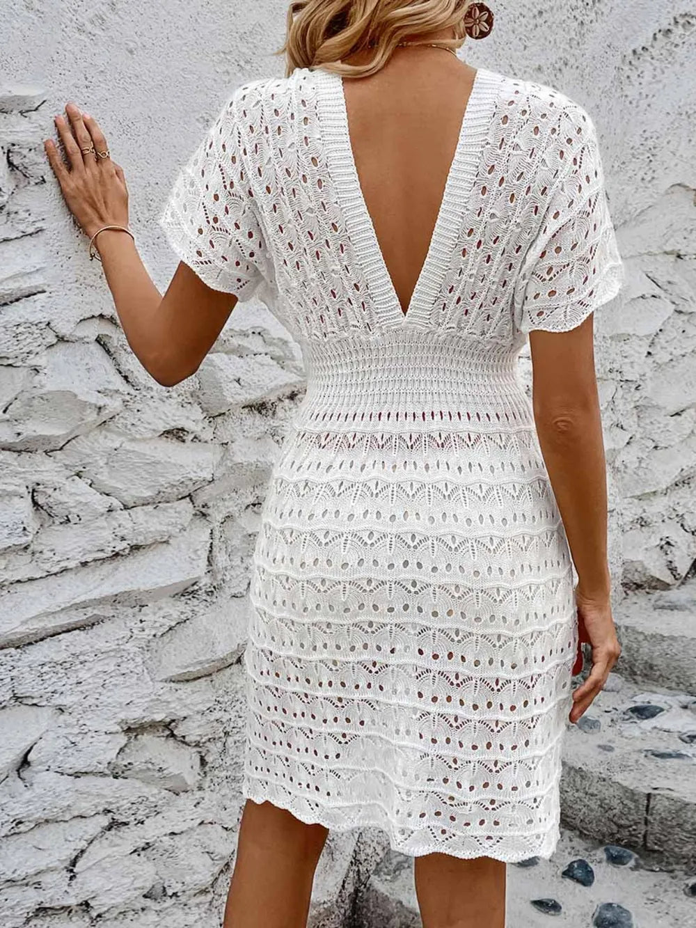 White lace dress with open back worn by a person against a stone wall.