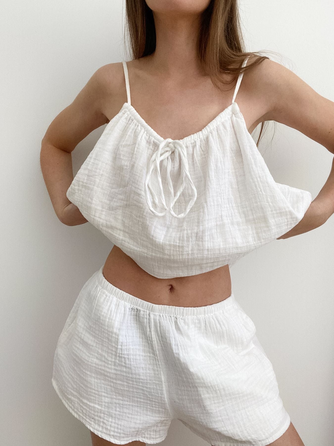 Person wearing a white top and shorts set against a plain background