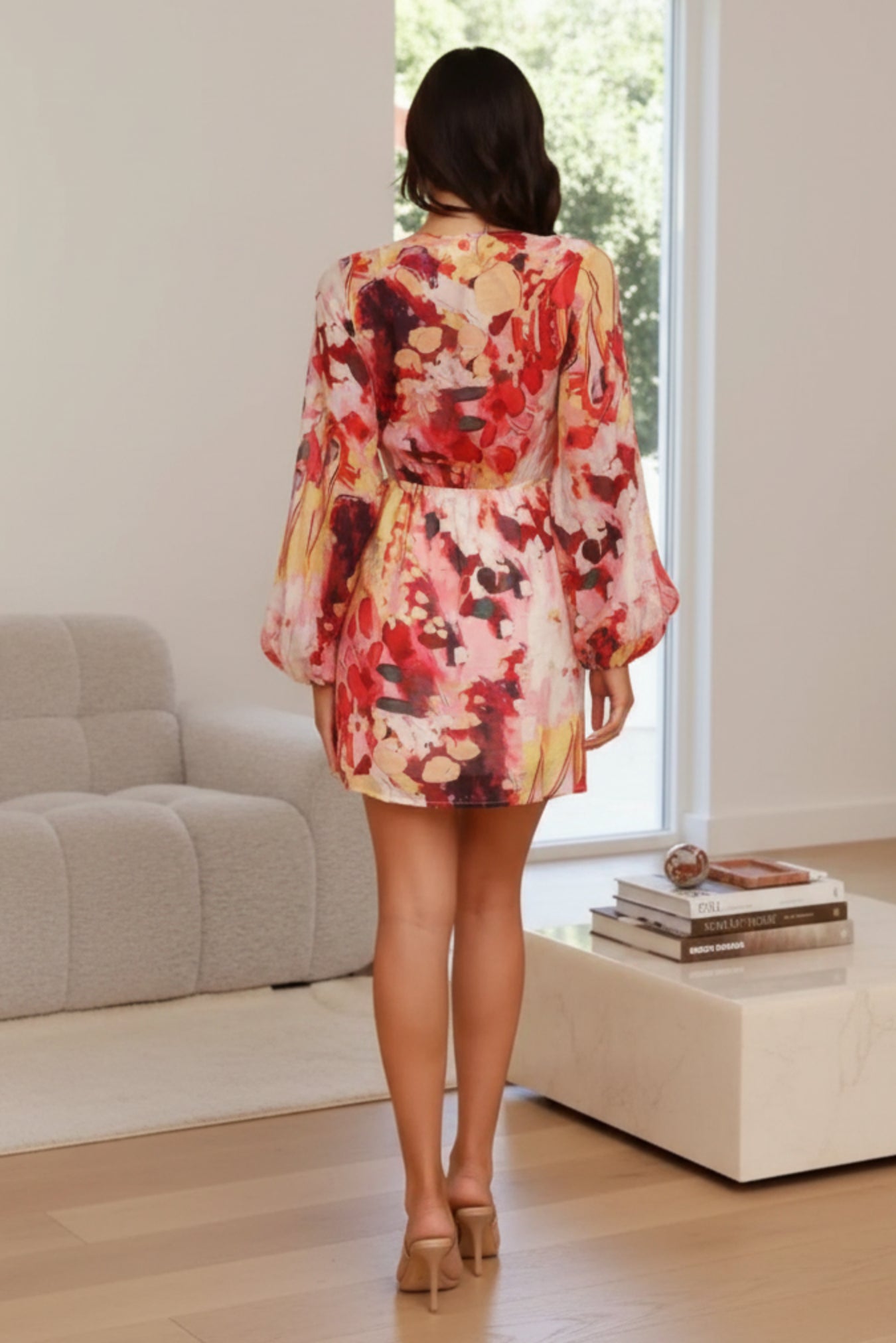 Woman wearing a colorful floral dress in a room with books and a couch.