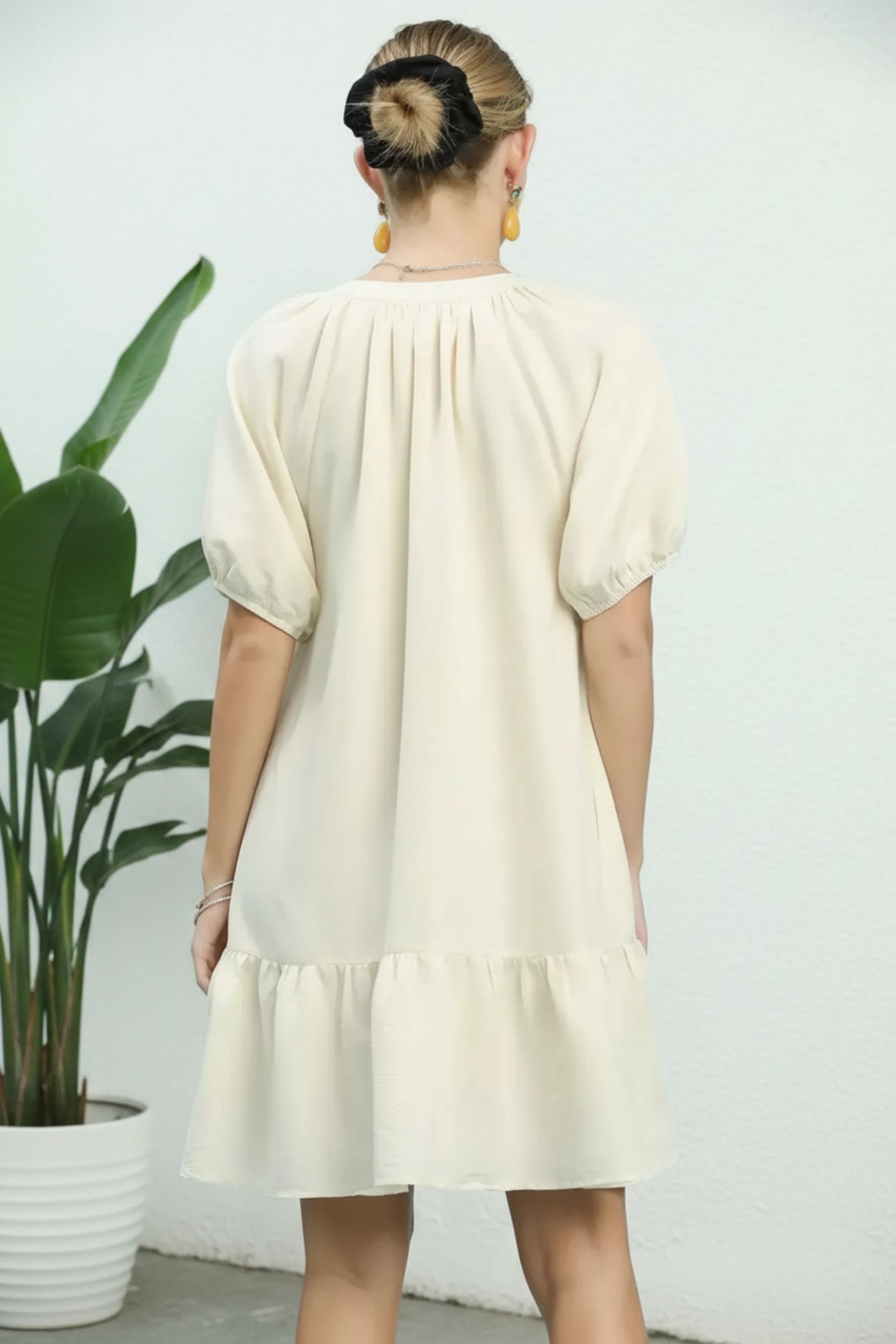 Woman wearing a white dress standing in front of a plant against a white wall