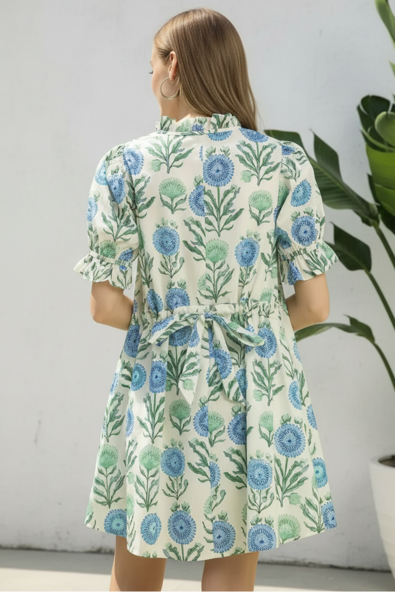 Woman wearing a floral dress with a white wall and plant background