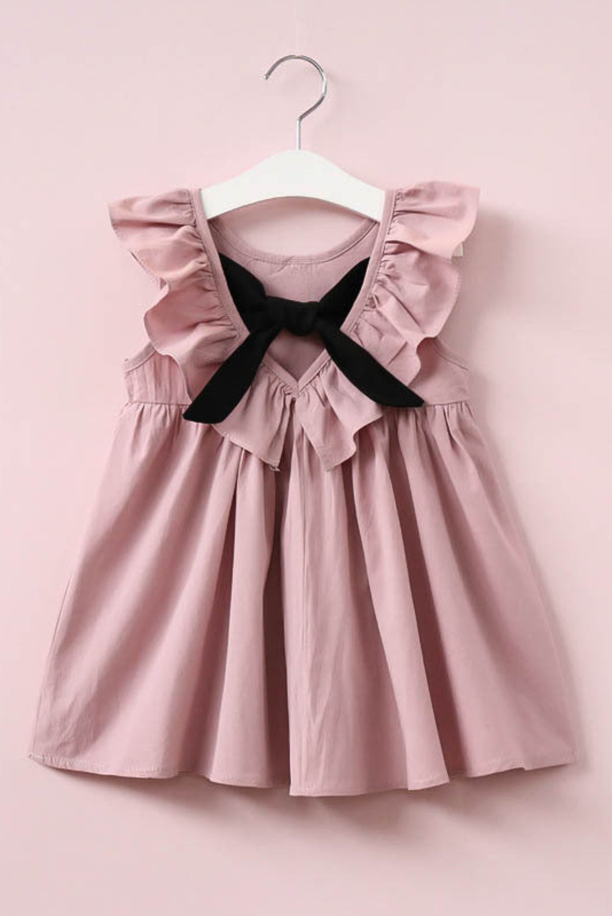 Pink dress with ruffled straps on a hanger against a pink background