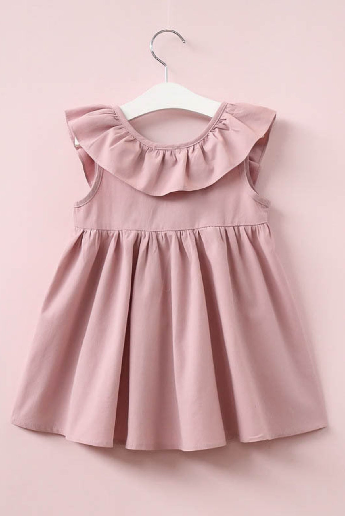 Pink dress with ruffled collar on a hanger against a pink background