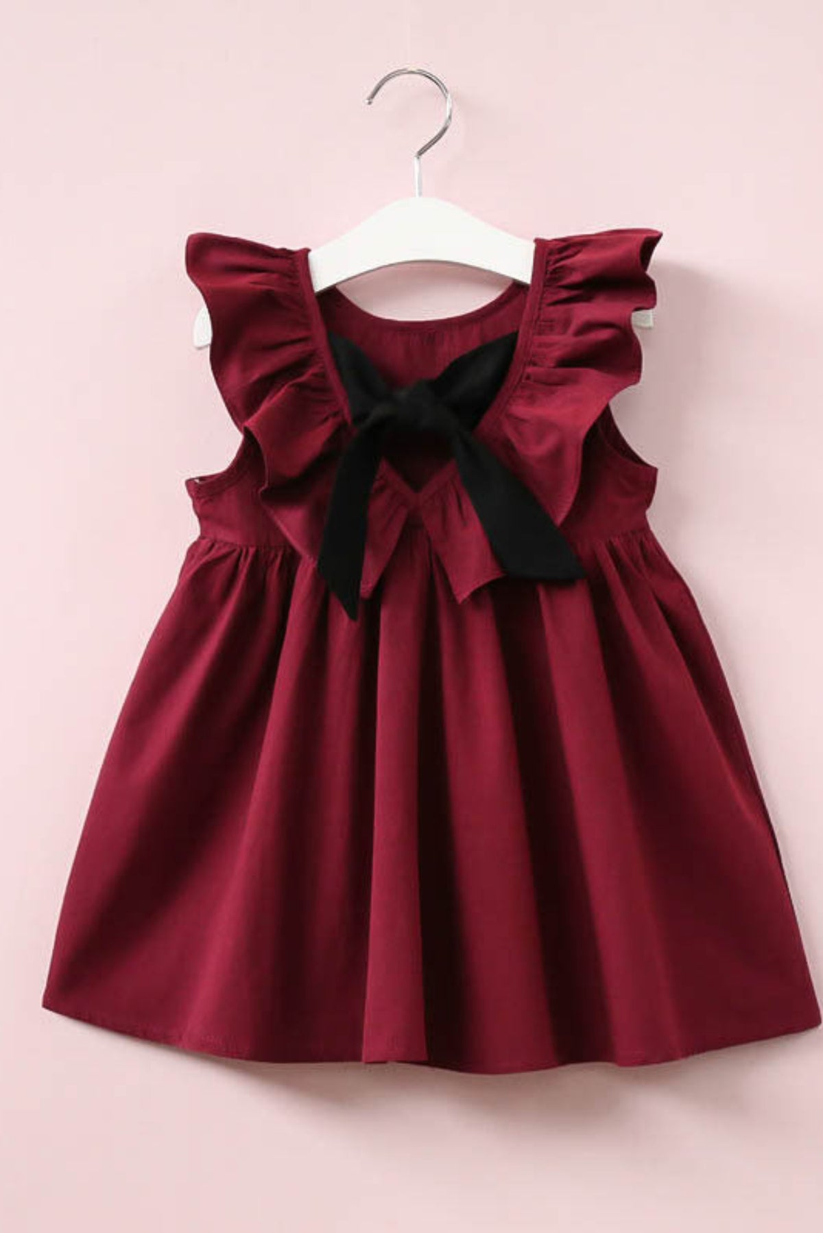 Red dress with black bow on a white hanger against a pink background