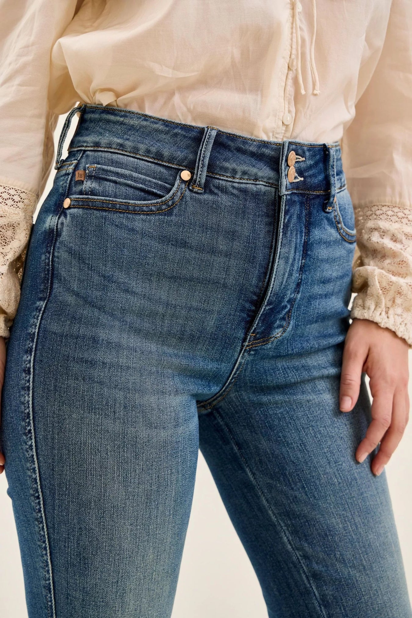Close-up of blue jeans with a beige shirt in a white background