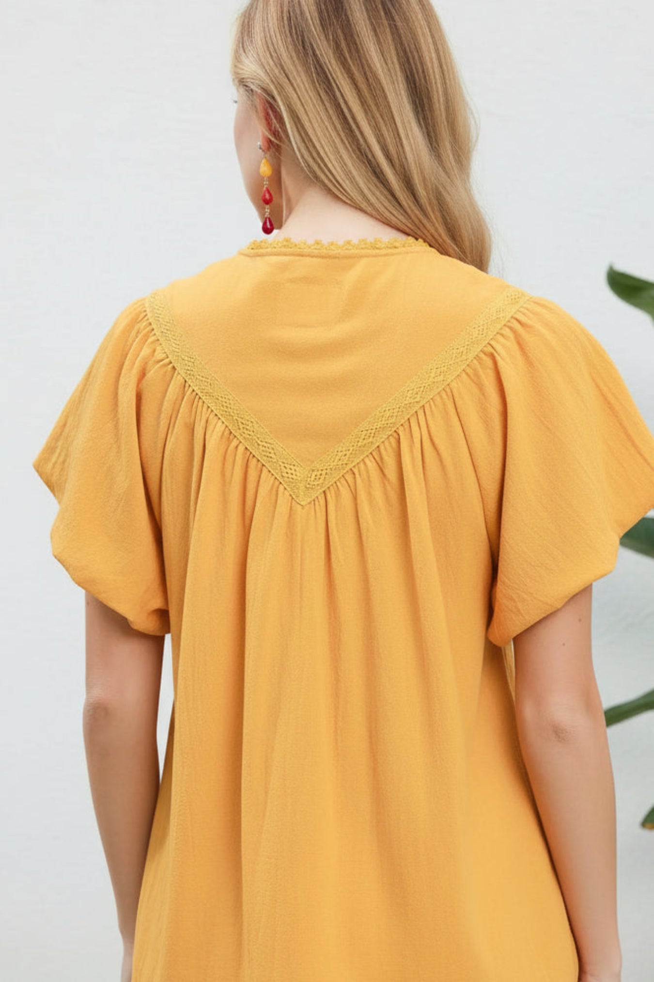 Yellow top with lace neckline worn by a person on a plain background
