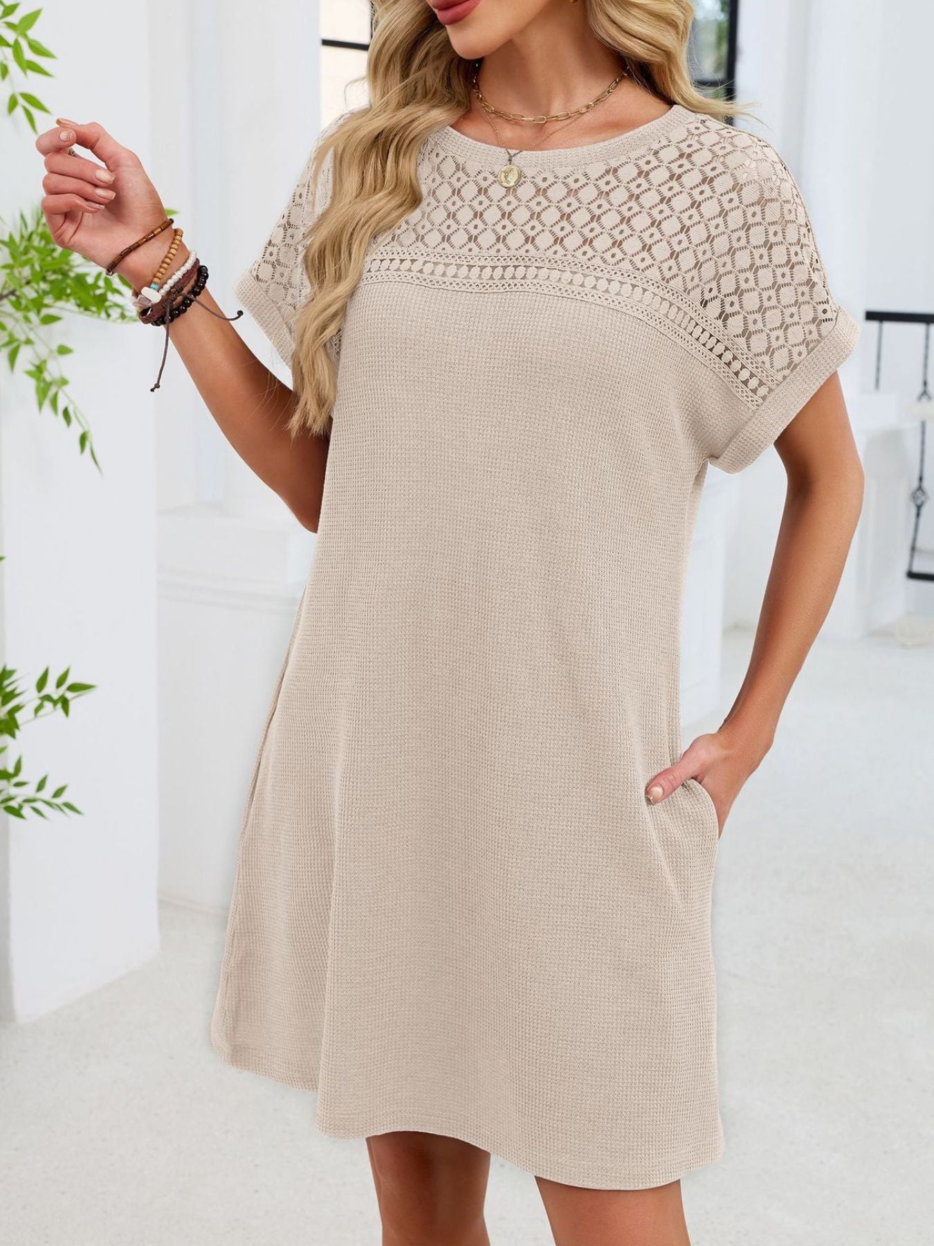 Woman wearing a beige dress with lace details in a bright room.