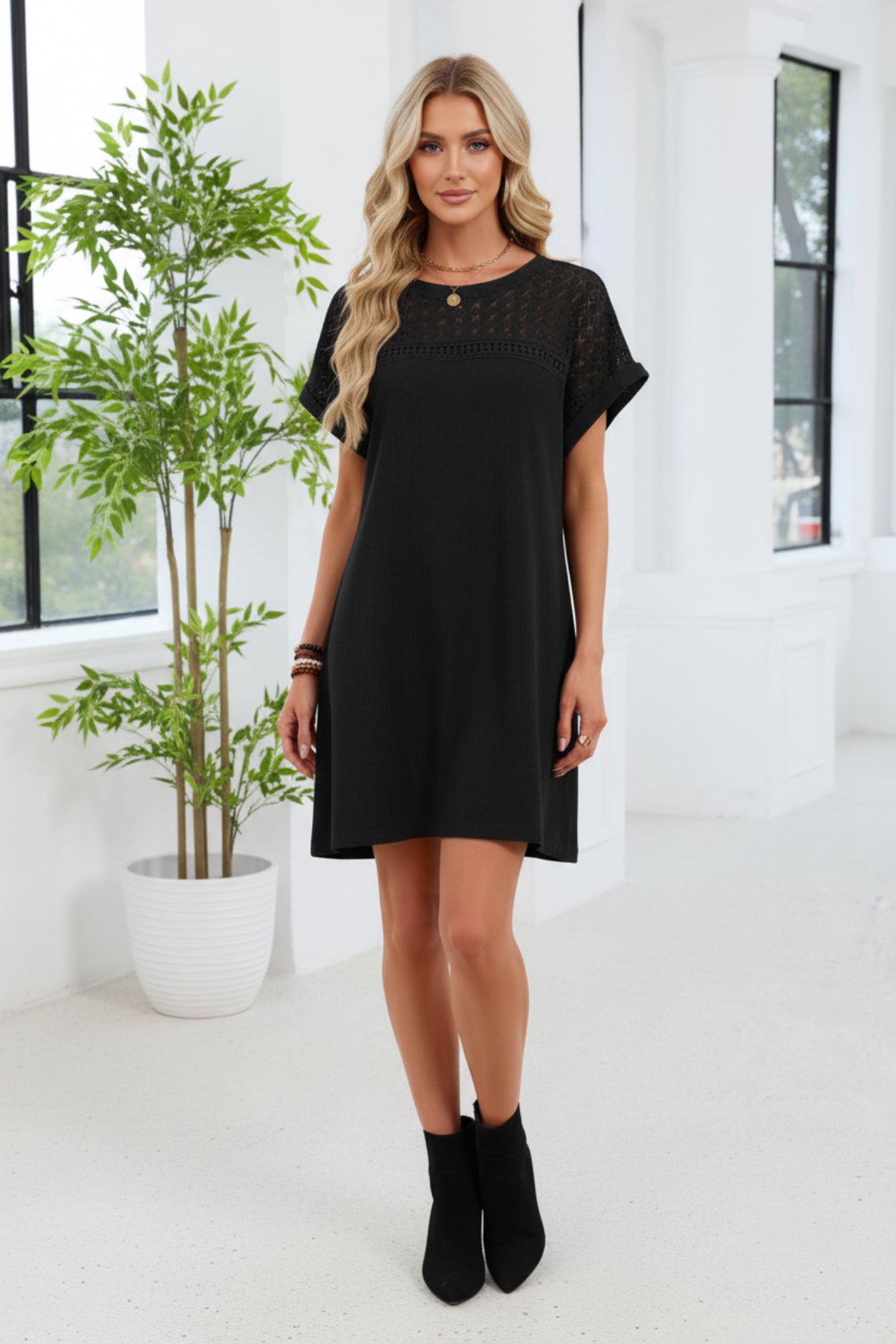 Woman wearing a black dress with lace details in an indoor setting.