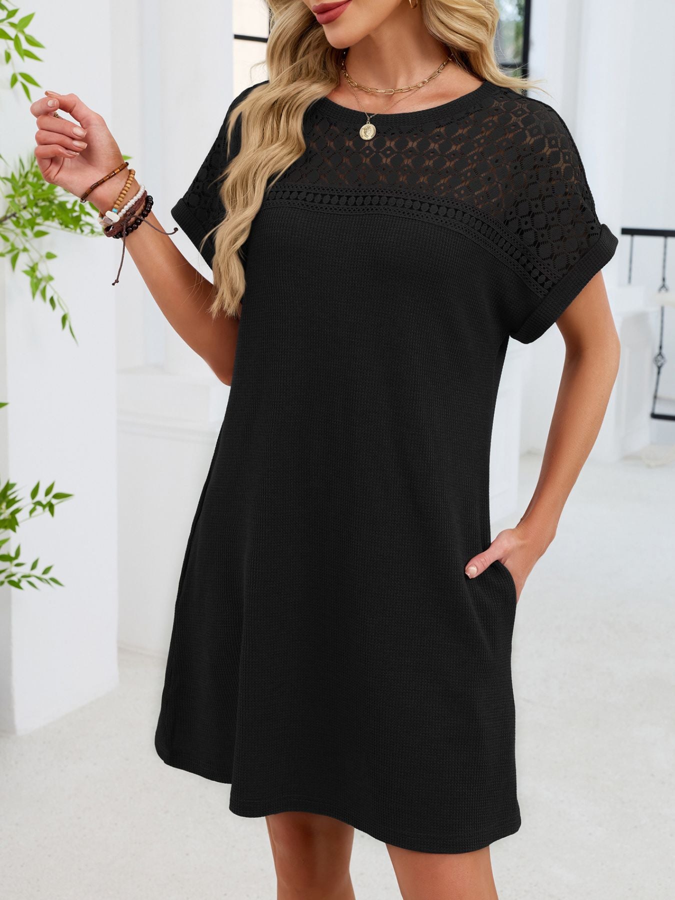 Woman wearing a black dress with lace details in a bright room.
