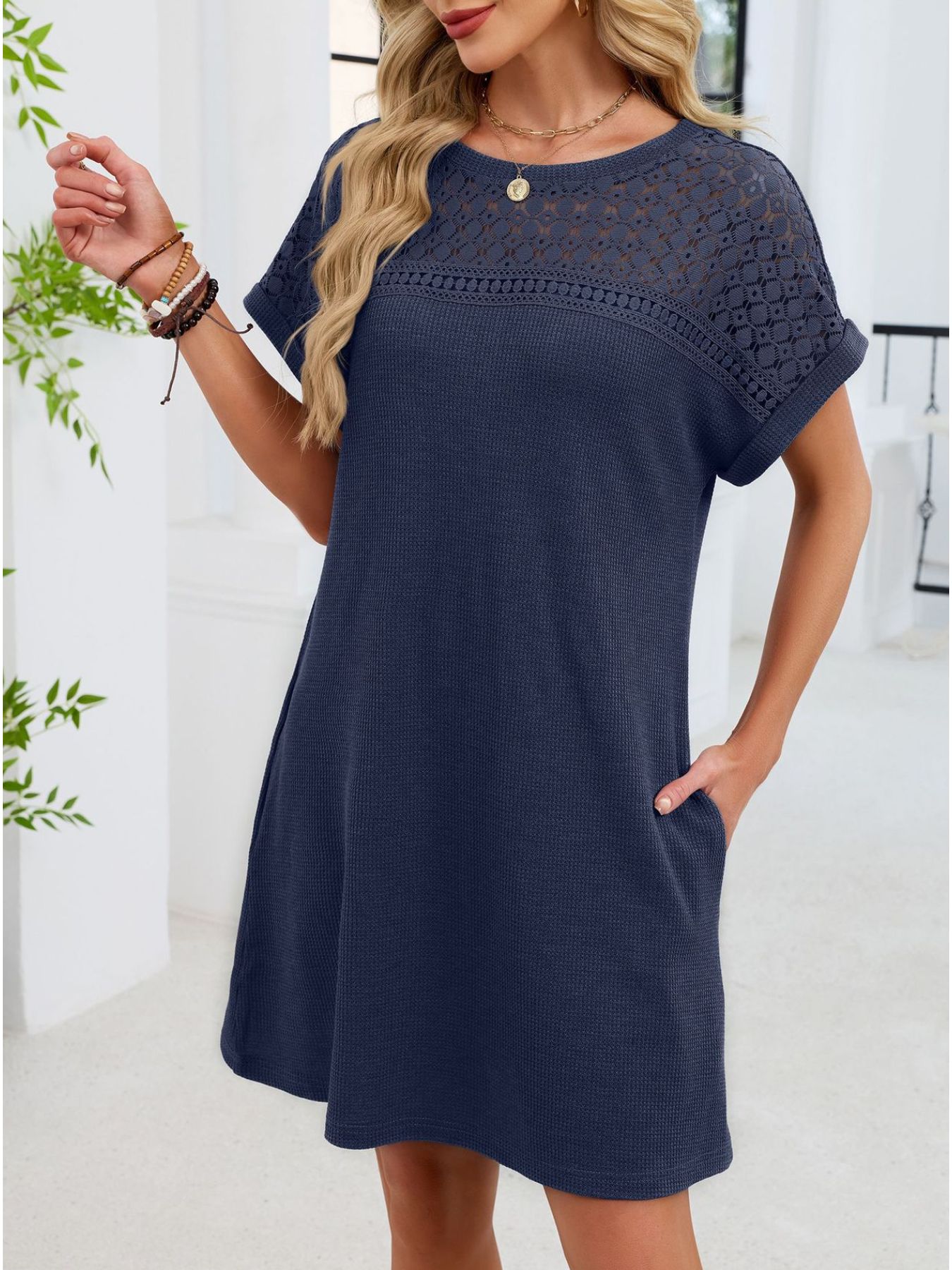 Woman wearing a navy blue dress with lace details in a bright room.