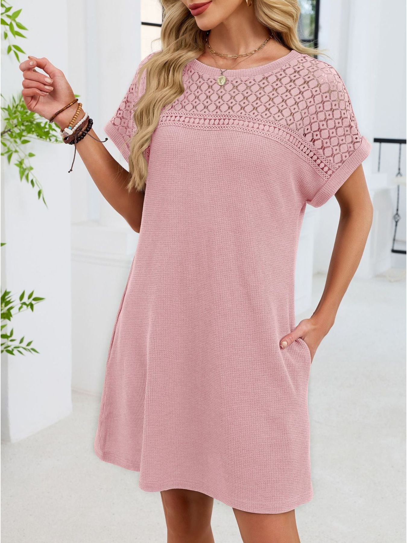 Woman wearing a pink dress with lace details in a bright room.