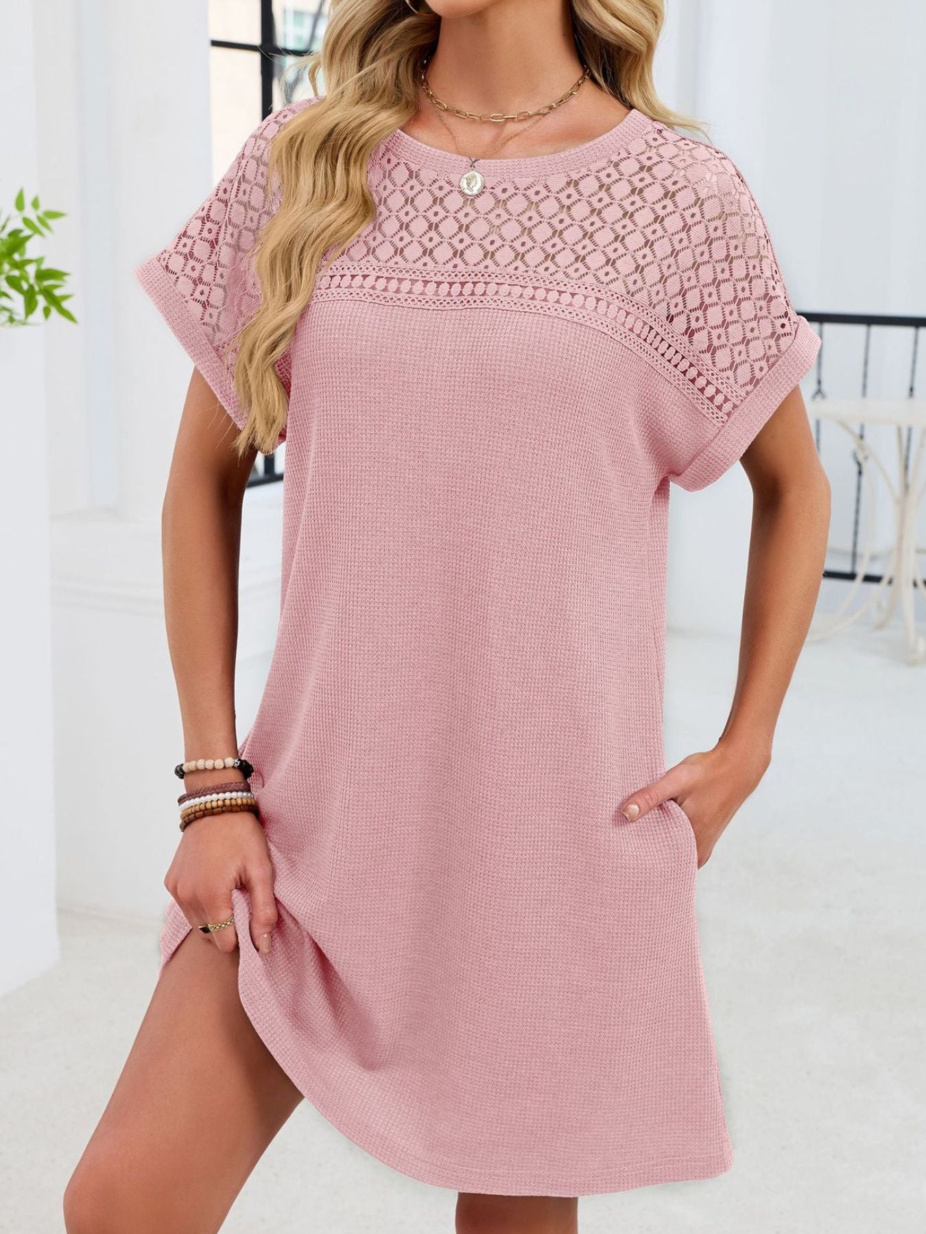 Woman wearing a pink dress with lace details in a bright room.