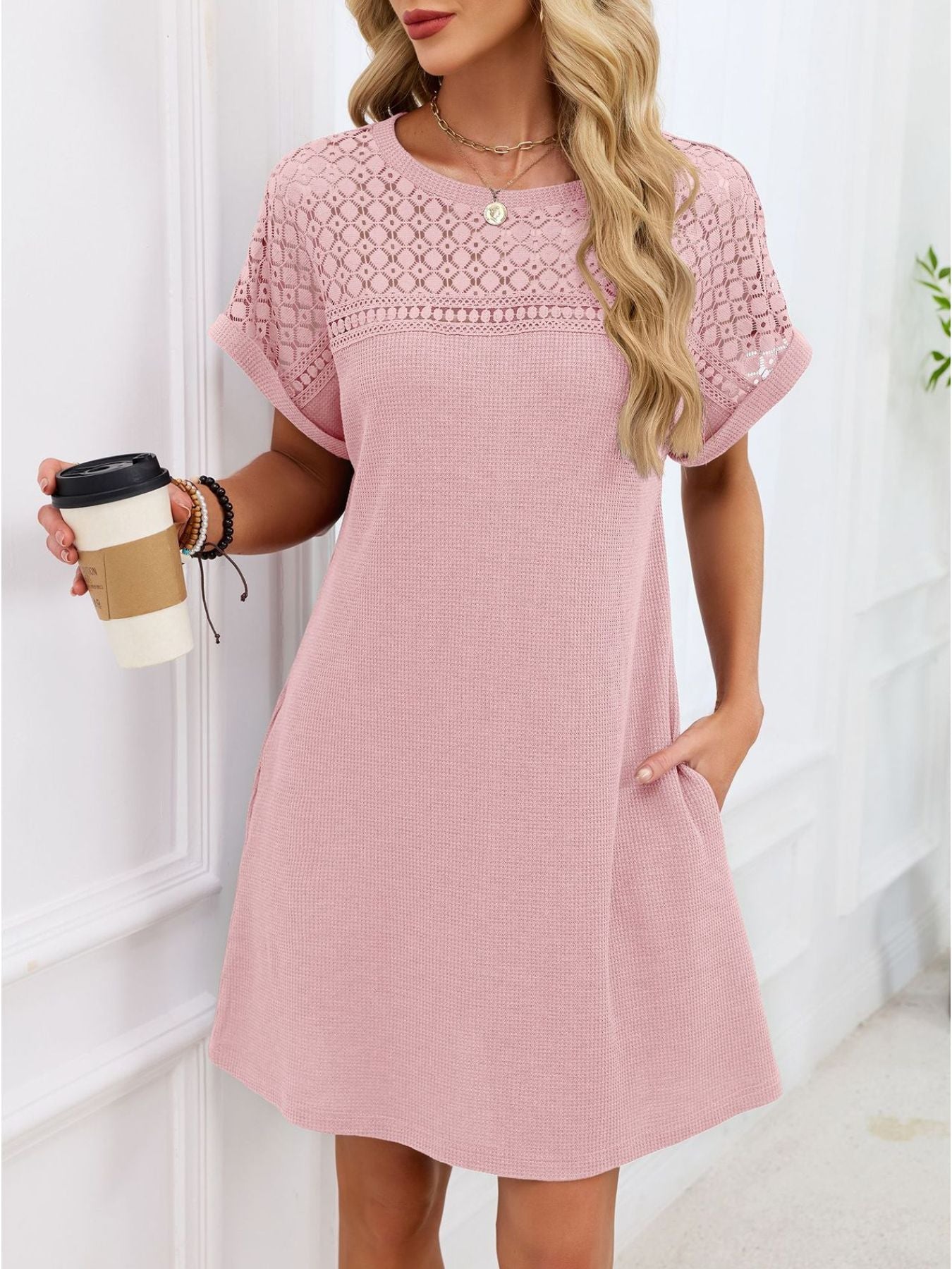 Woman wearing a pink dress with lace details, holding a coffee cup indoors.