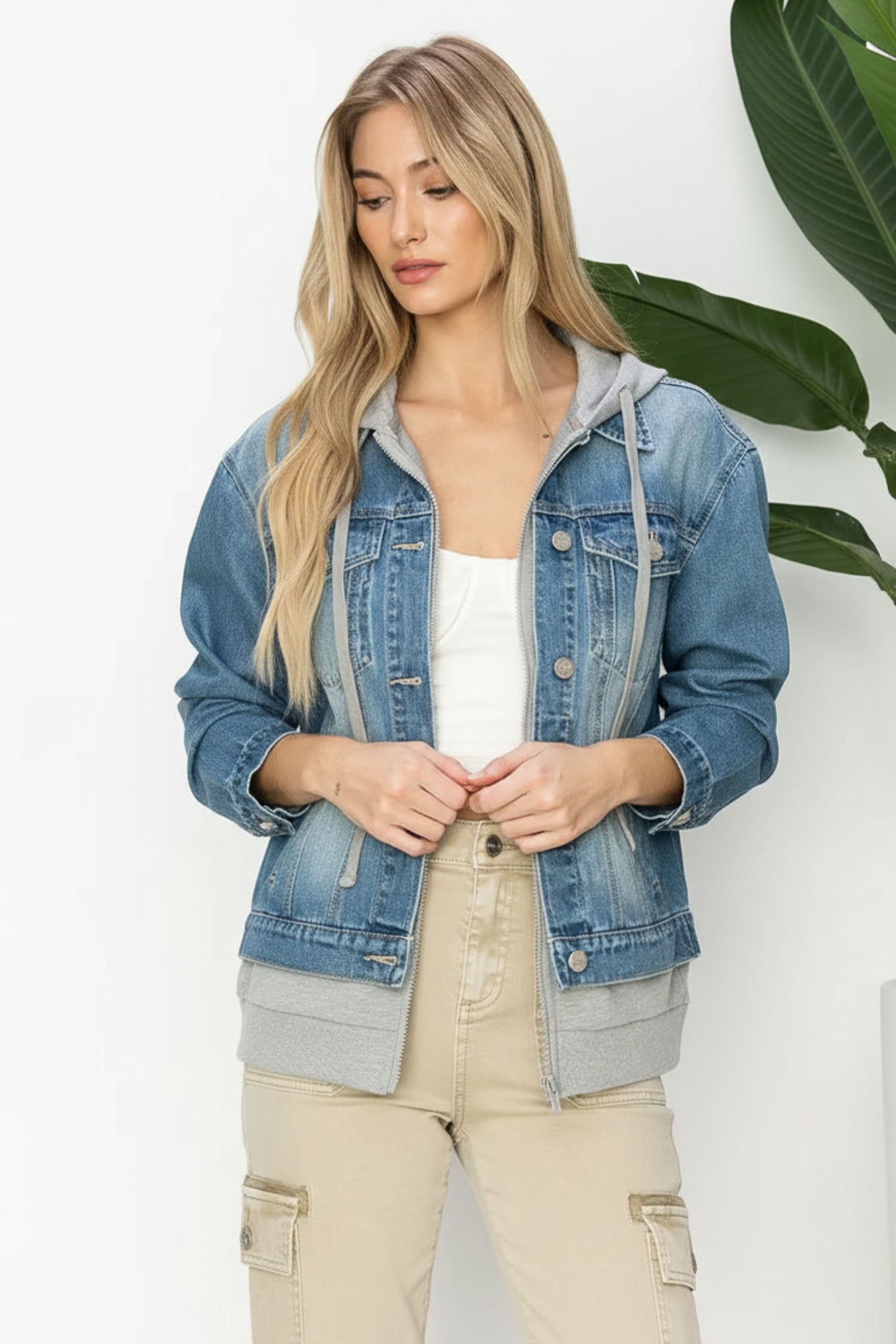 Woman wearing a denim jacket over a white top and beige pants on a white background