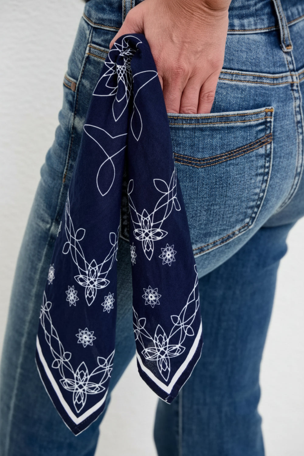 Navy blue bandana with white patterns held by a person wearing blue jeans.