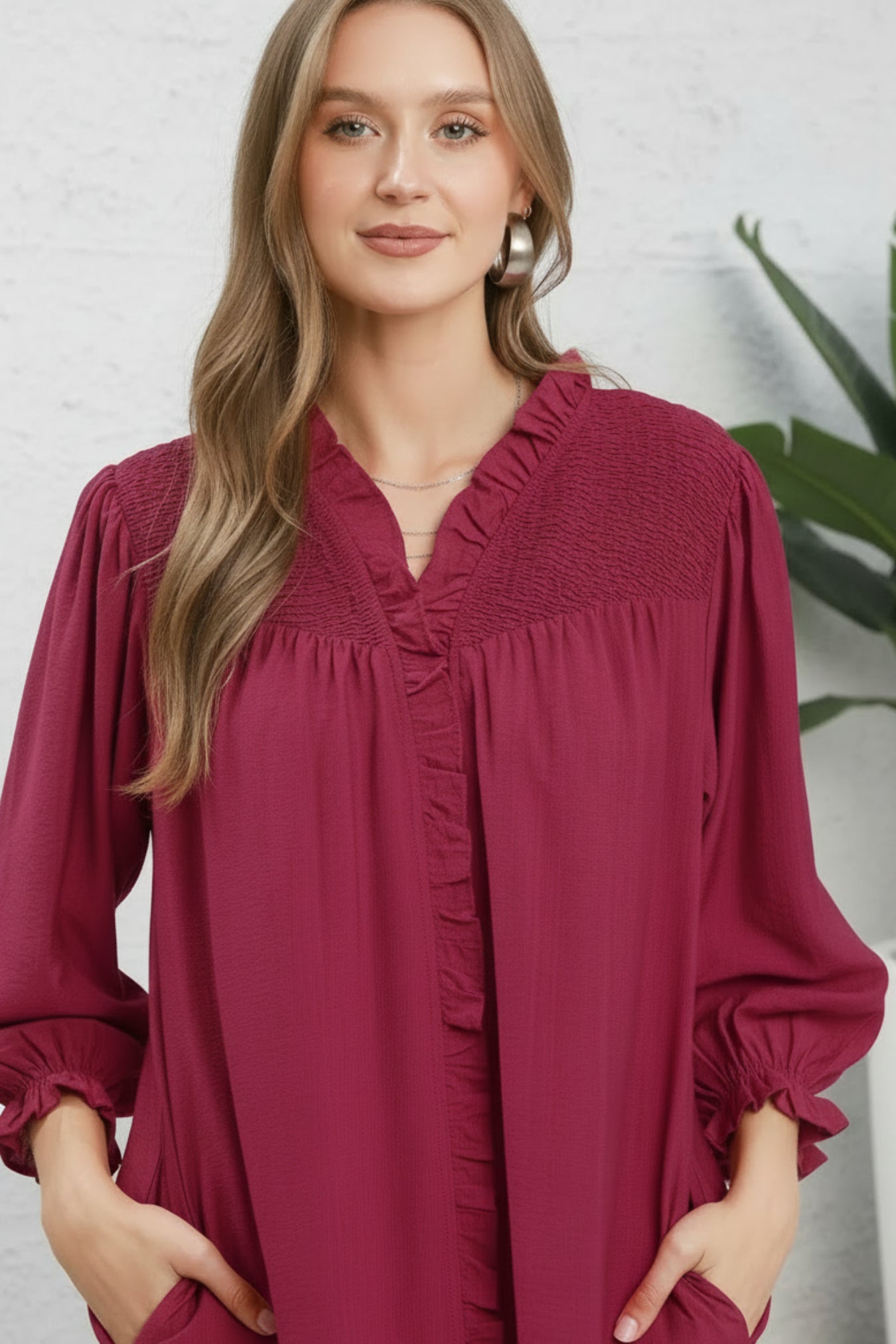 Woman wearing a maroon blouse with smocked details on a white background