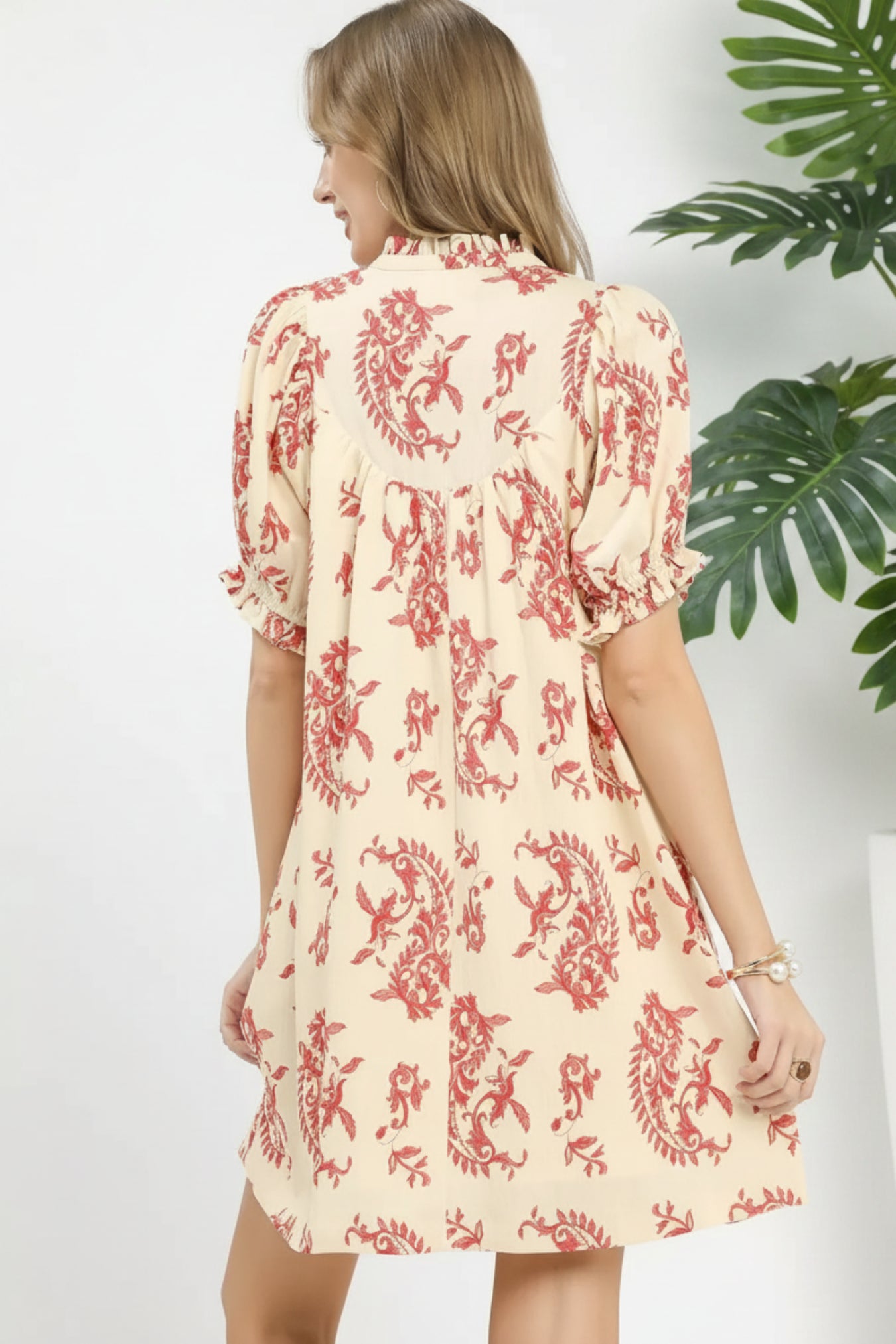 Woman wearing a cream dress with red floral pattern on a white background