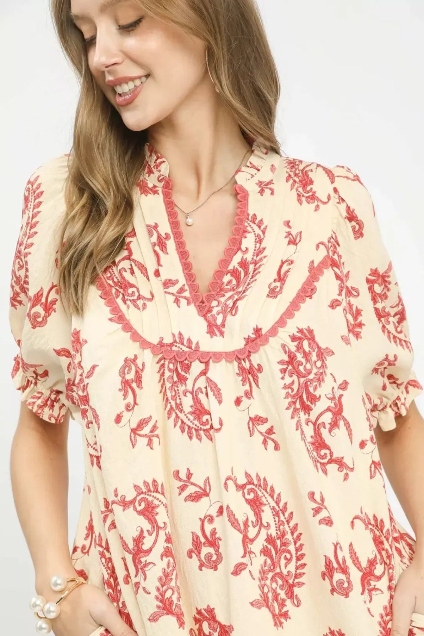 Woman wearing a cream dress with red floral embroidery on a white background