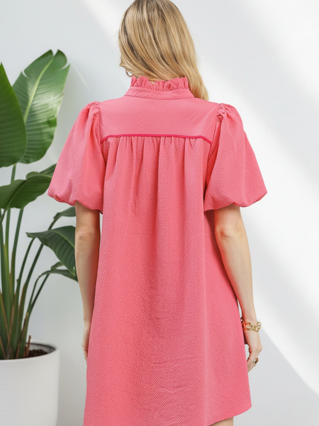 Woman wearing a pink dress with puff sleeves against a white background