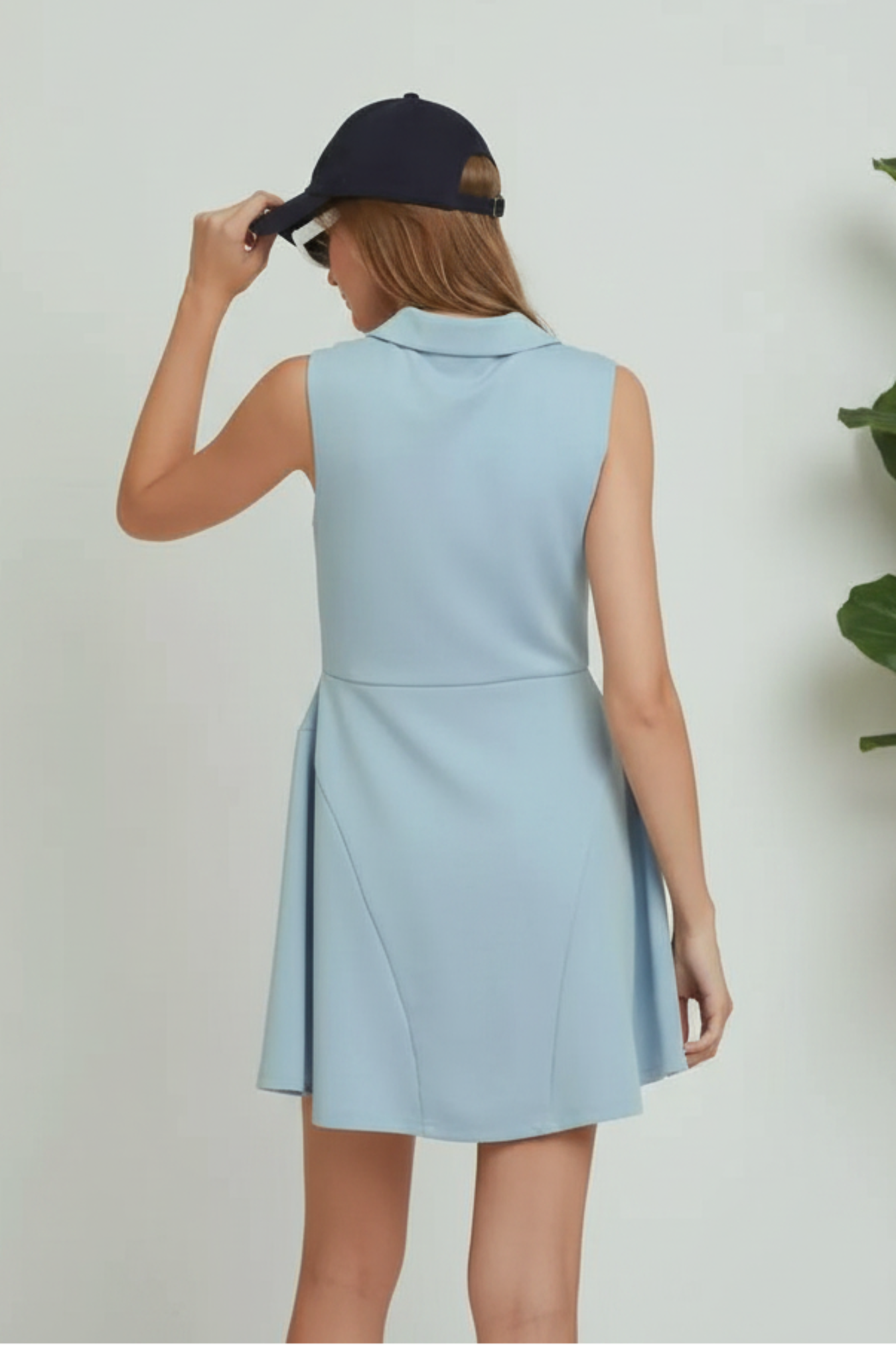 Woman wearing a light blue sleeveless dress with a navy cap on a plain background