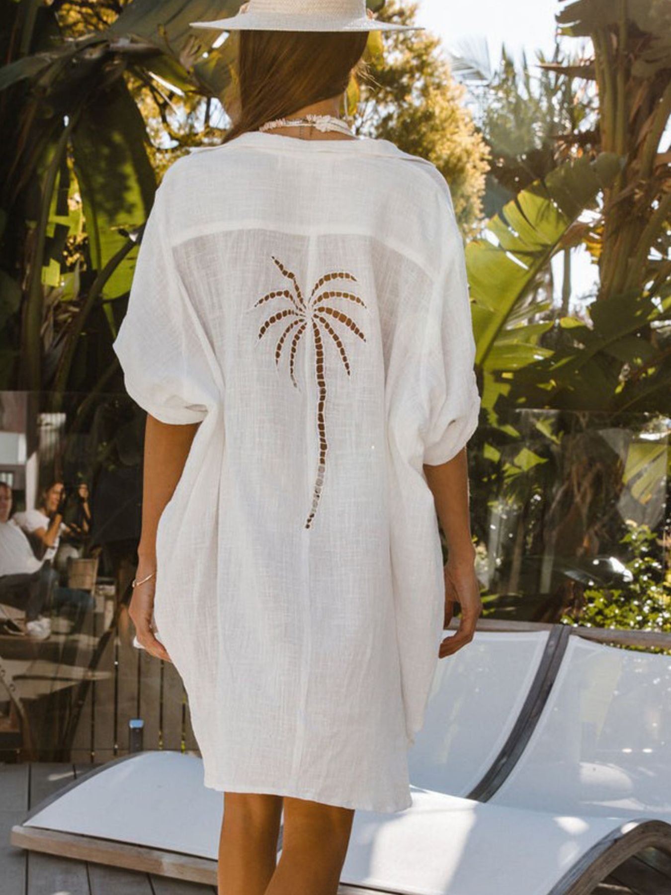 Person wearing a white cover-up with a palm tree design in a tropical setting