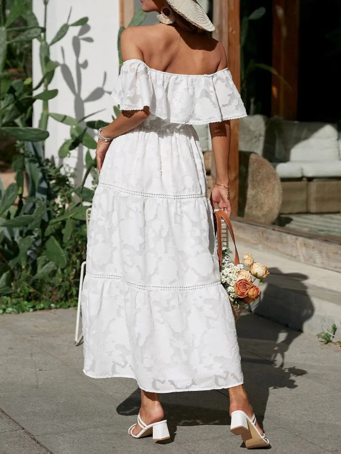 Woman in a white off-shoulder dress holding a bouquet of flowers outdoors.