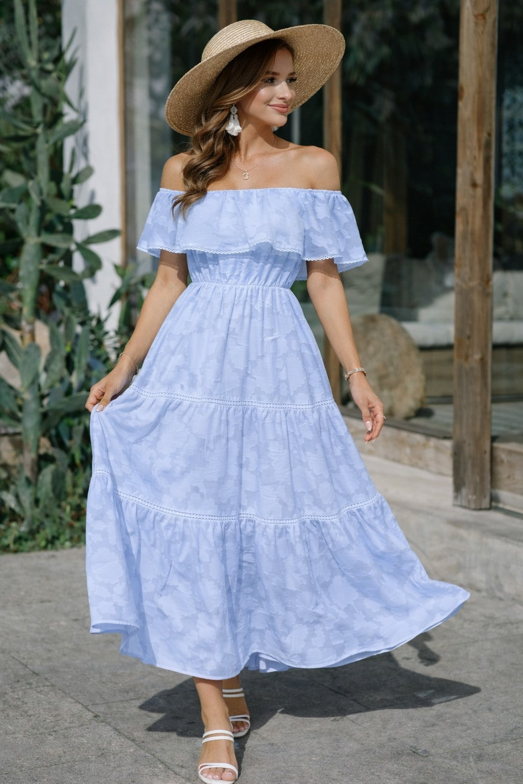 Woman wearing a light blue off-shoulder dress and straw hat outdoors.