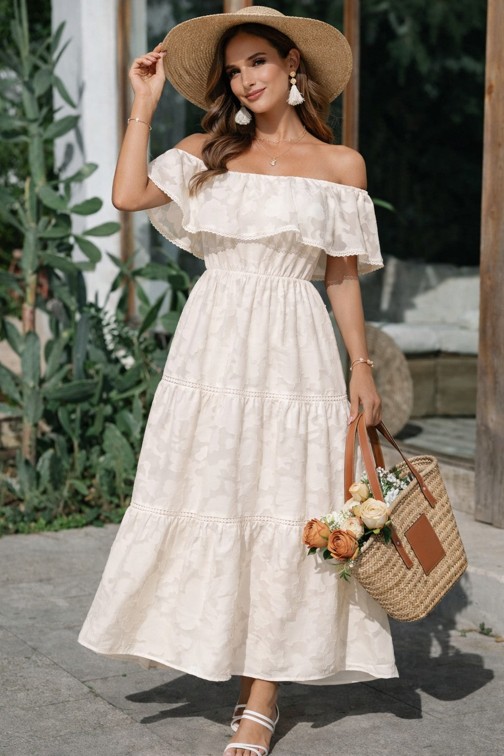 Woman in a white off-shoulder dress with a straw hat and bag, standing outdoors.