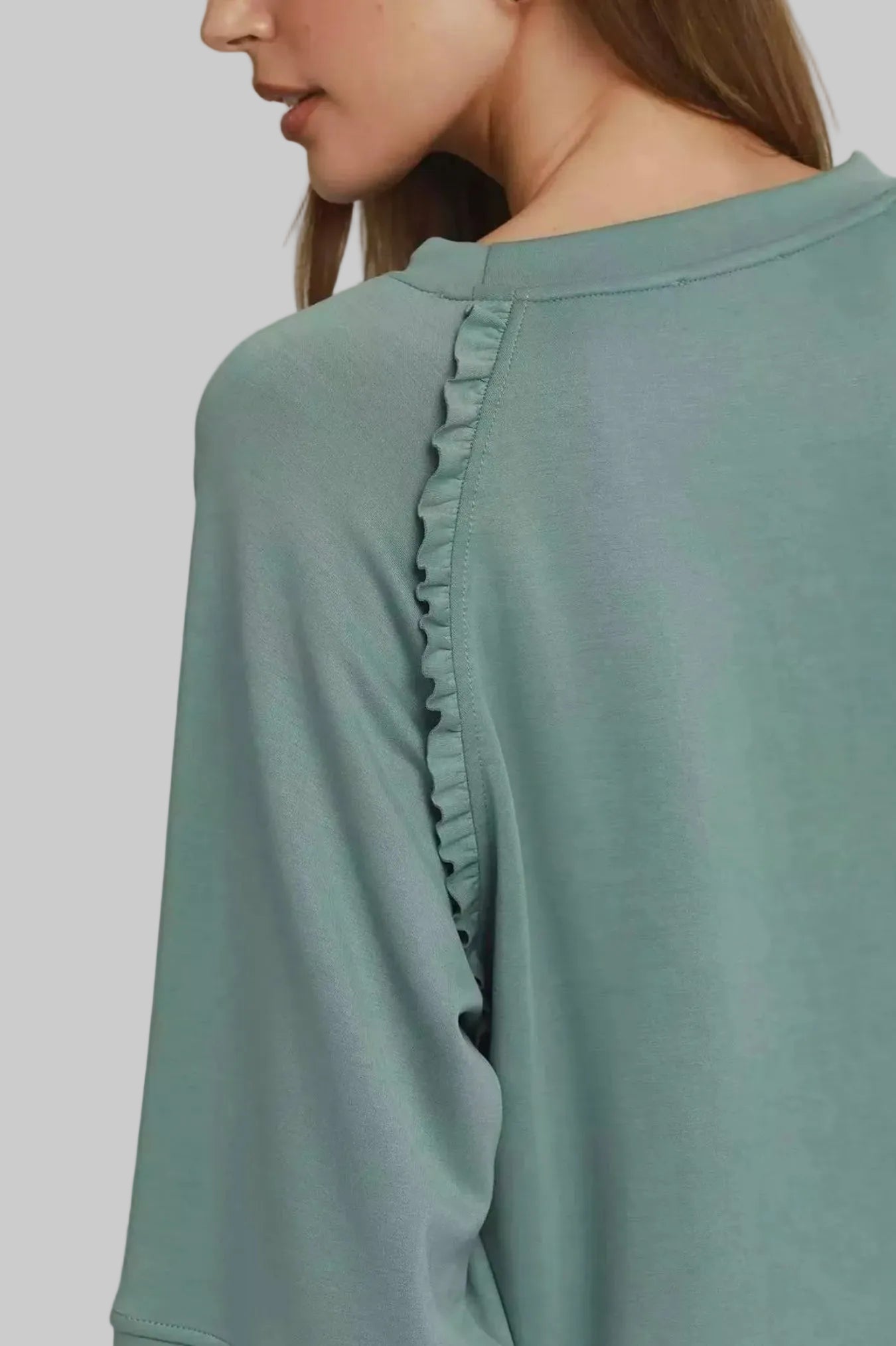 Close-up of a person wearing a light green long-sleeve top with ruffled details on a white background.