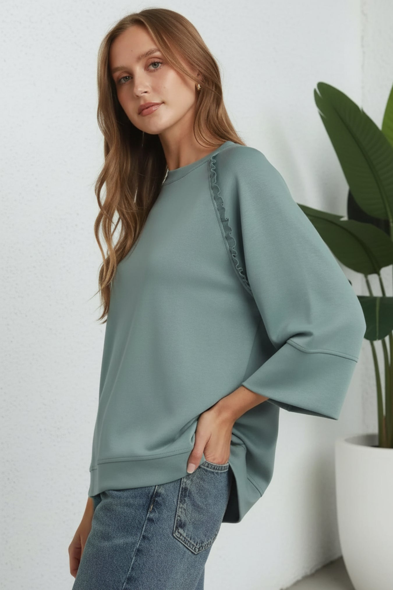 Woman wearing a light green sweater and jeans on a white background with plant