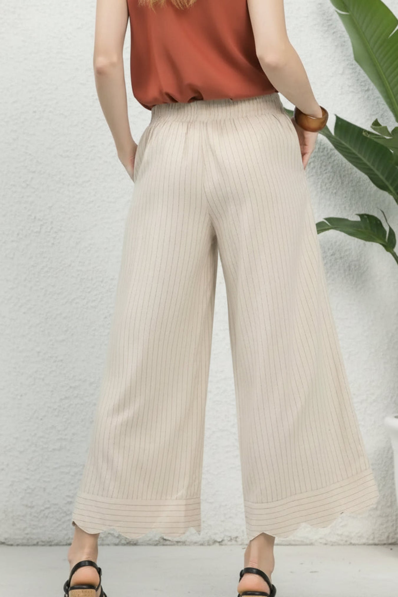 Person wearing beige wide-leg pants and a rust-colored top against a white wall.