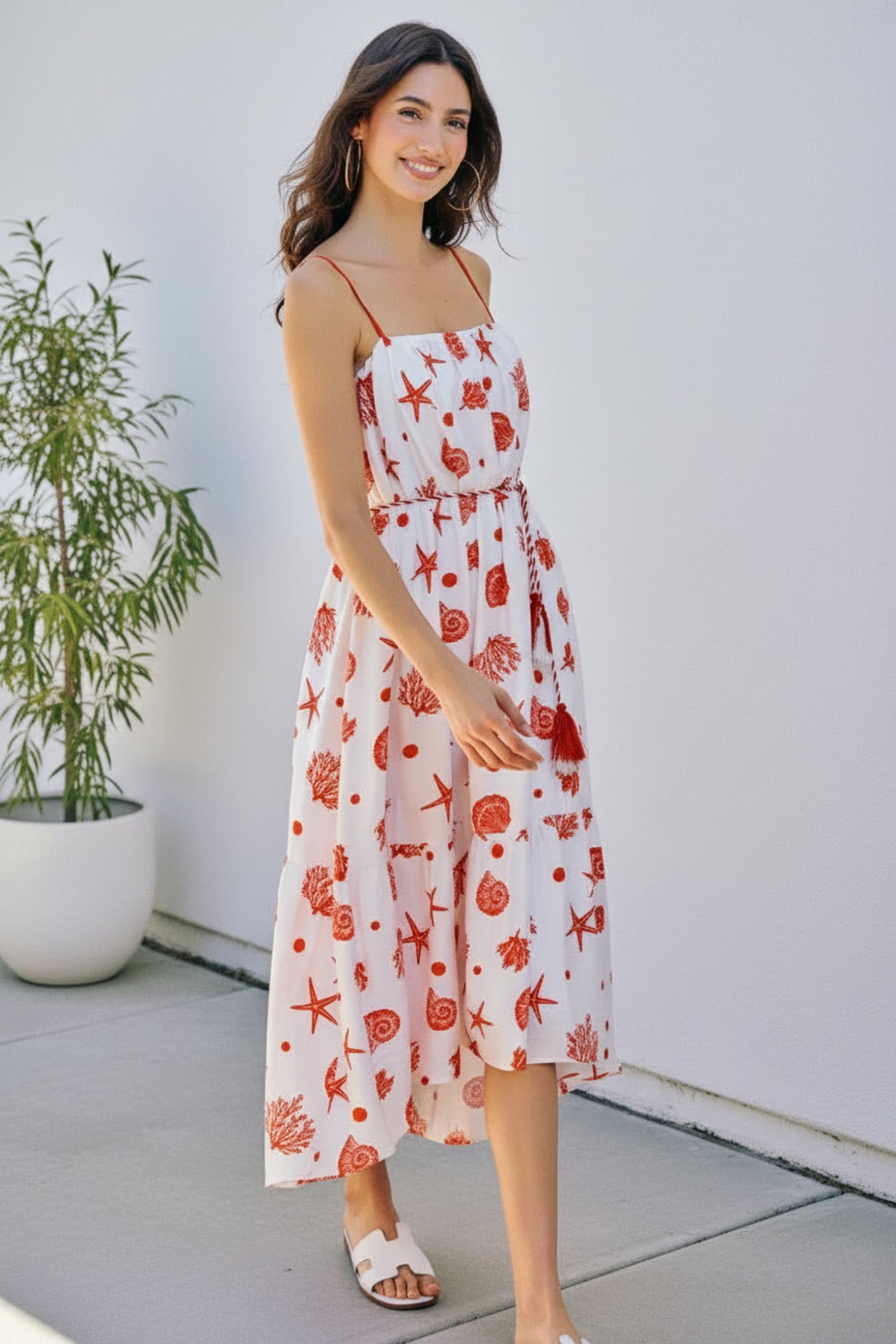 Woman in a white dress with red floral pattern standing outdoor.